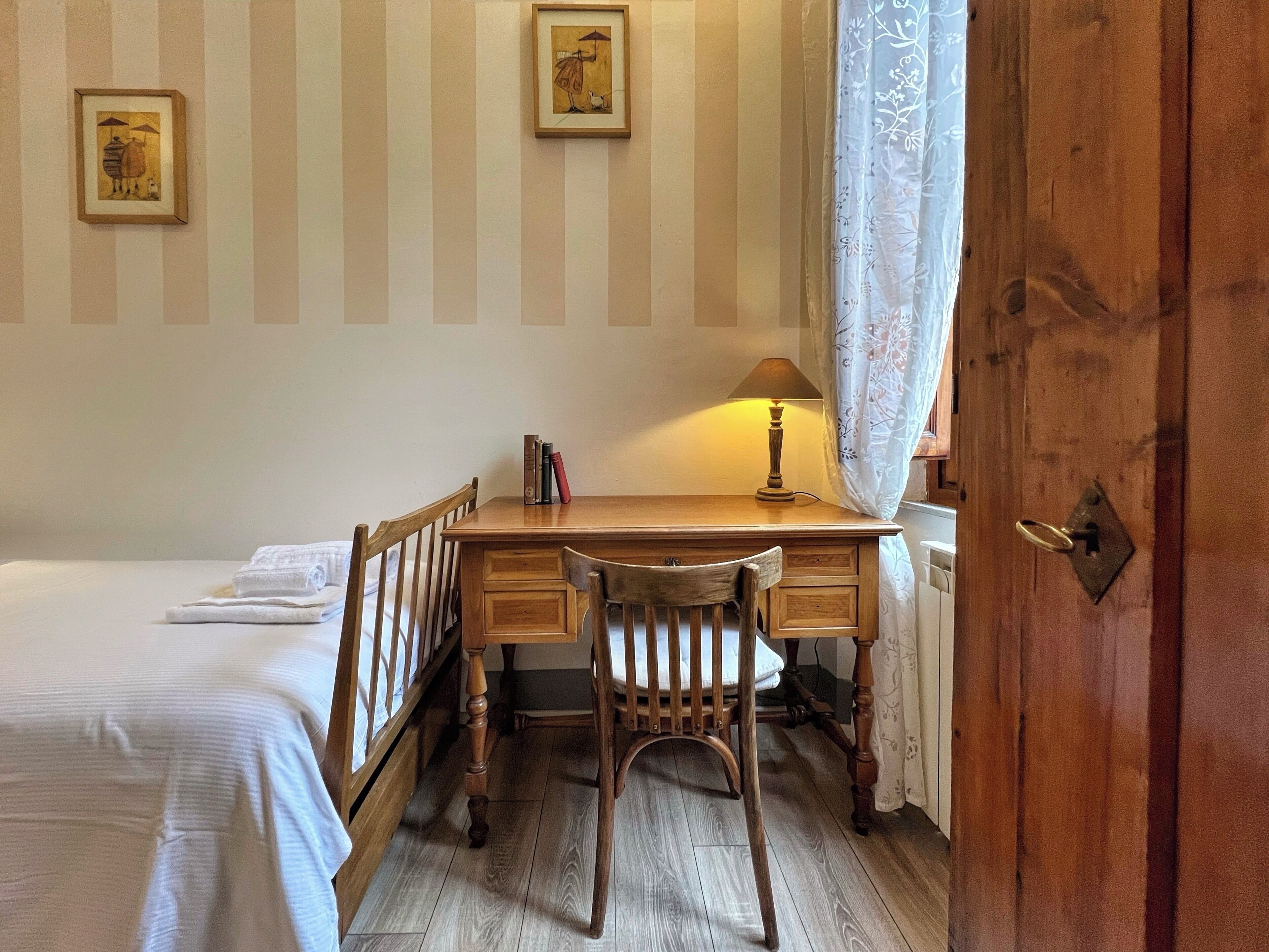 Une petite pièce agréable et chaleureuse, avec un bureau en bois, une chaise, un lit et deux tableaux encadrés accrochés au mur.
