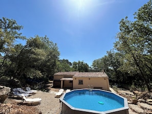 An outdoor swimming pool with lounge chairs, a small building, and surrounding trees. - Air-conditioned family home with SWIMMING POOL and SPA.At the edge of the forest (Le Luc)