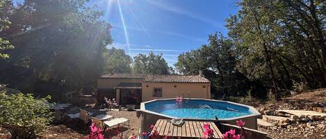 A swimming pool with a wooden deck, surrounded by pink flowers and trees.