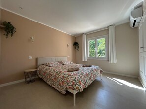 A bedroom with a bed, a window, a plant, and an air conditioning unit.