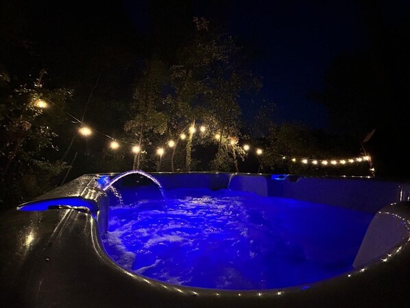 A swimming pool with a water slide, surrounded by trees and string lights.