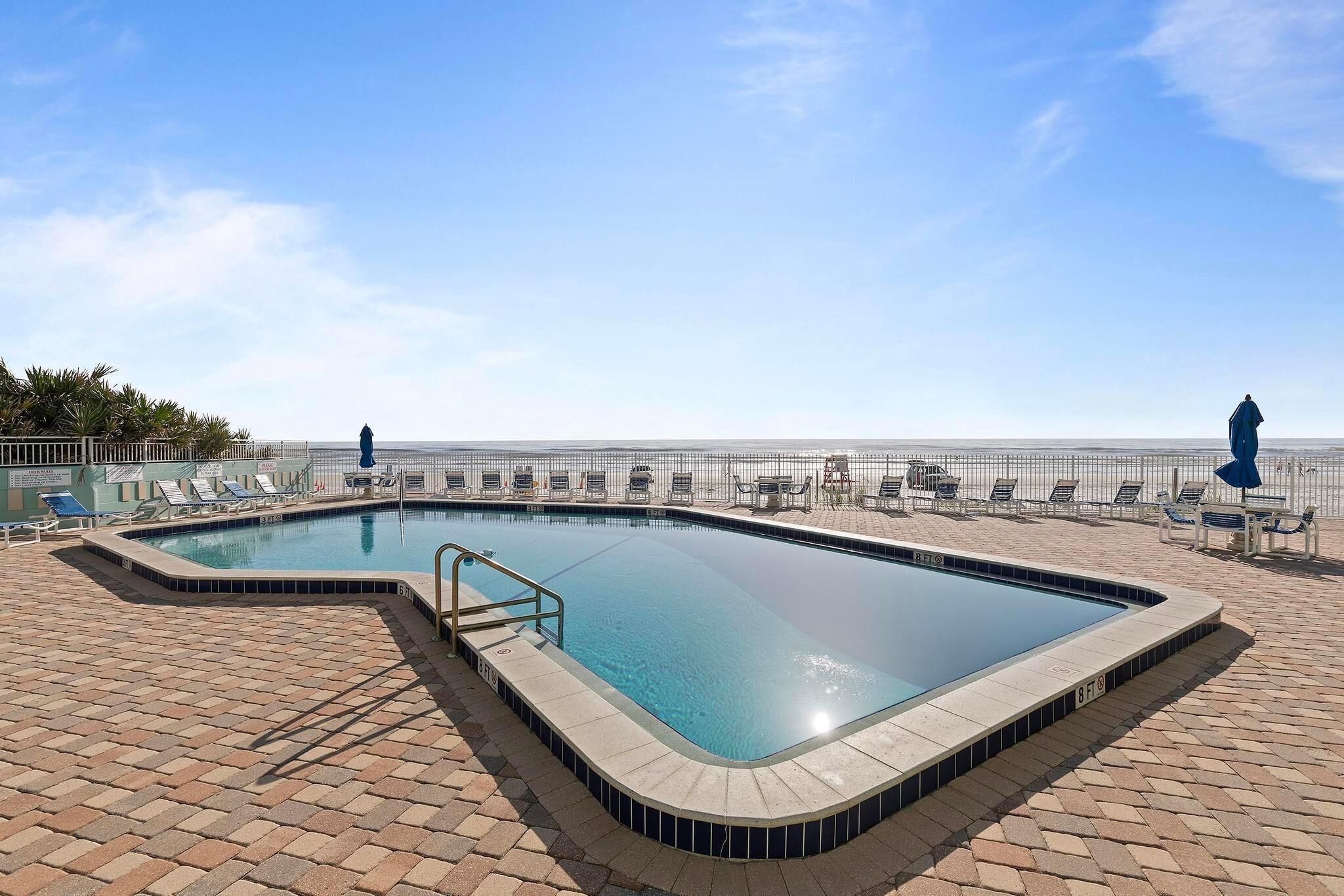 A rectangular swimming pool with a tiled edge, surrounded by lounge chairs and umbrellas, with a clear sky above.