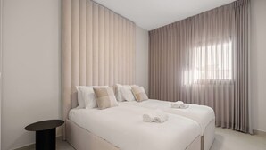 Une chambre d’hôtel moderne avec un grand lit, une petite table de chevet et une fenêtre avec des rideaux.