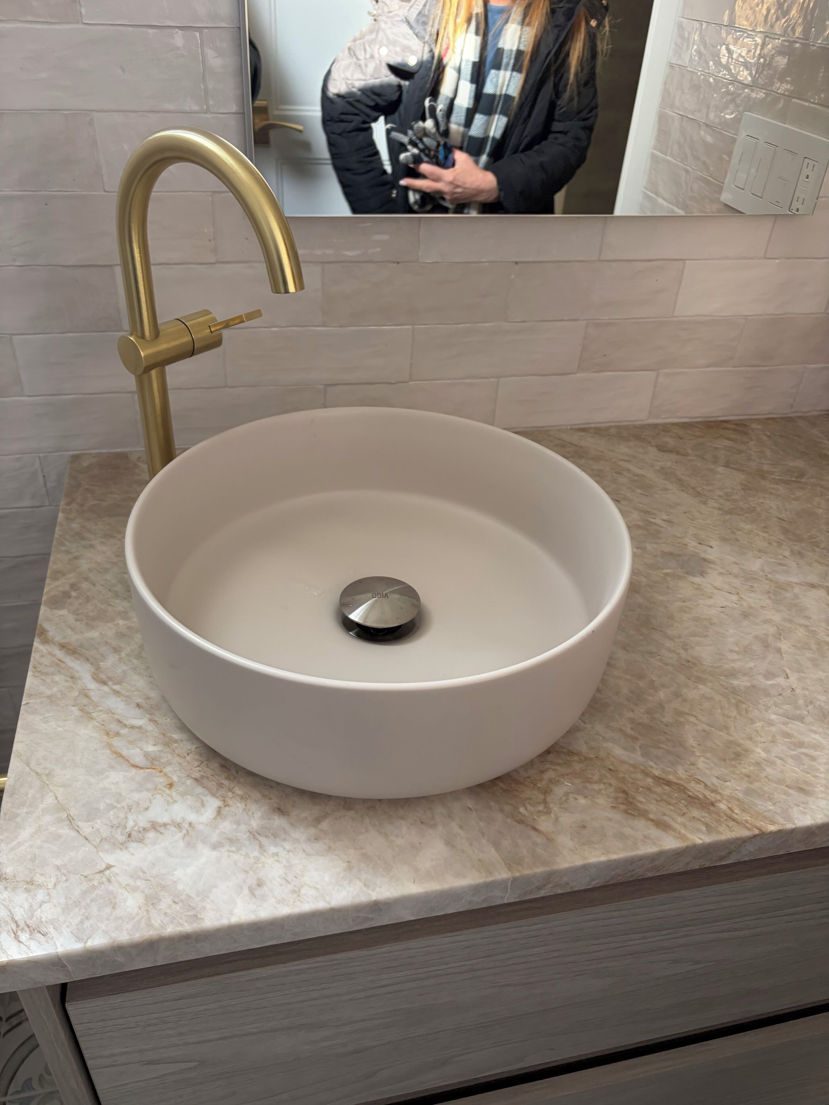 Een badkamer met een rond wastafel, een gouden kraan en een marmeren aanrechtblad.