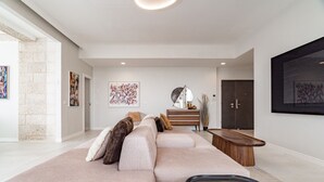 Un salon moderne avec un grand canapé d’angle, une table basse en bois et un téléviseur à écran plat fixé au mur.