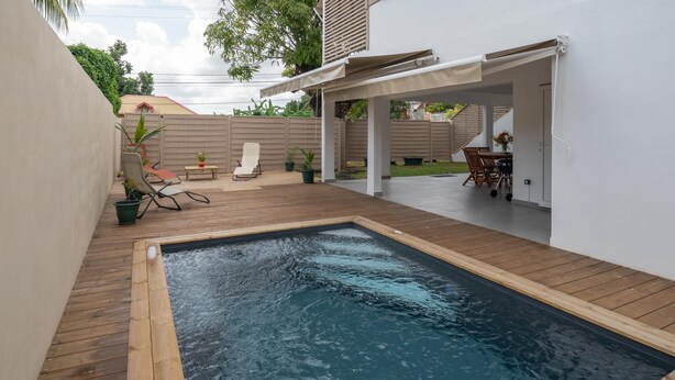 Een achtertuin met een zwembad, een houten terras, buitenzitplaatsen en een overdekte patio.