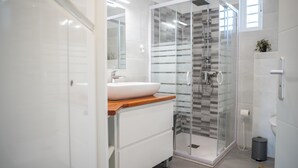 Un baño moderno con ducha de vidrio, un lavamanos blanco y una encimera de madera, y un espejo sobre el lavamanos.