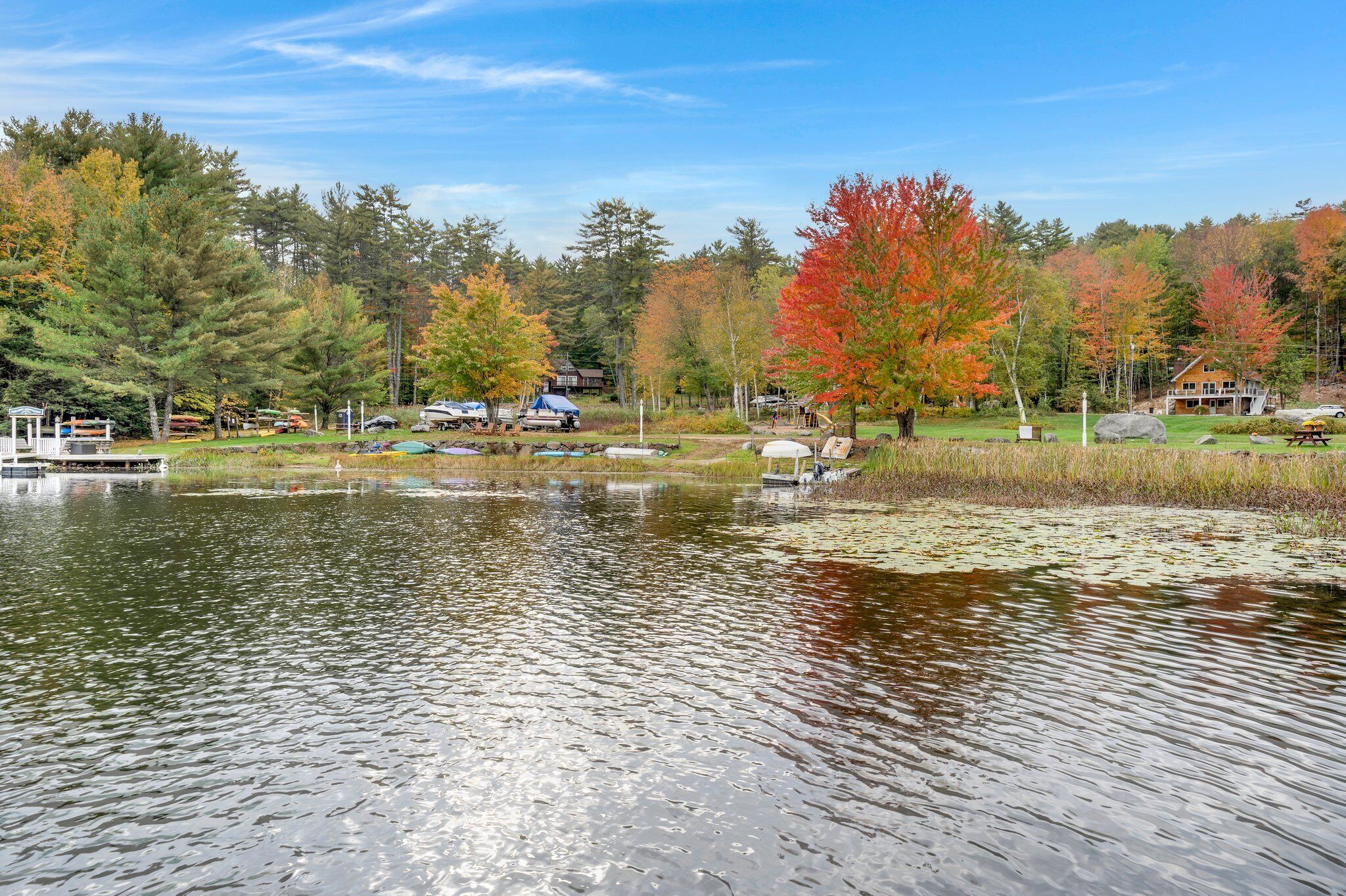 A lakeside view with a dock, picnic area, and cabins in a forested area.