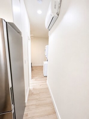 A narrow hallway with a stainless steel refrigerator on the left and a white washing machine on the right. - Walk to BYU Stadium - 1BR Guest House + Parking (Provo)
