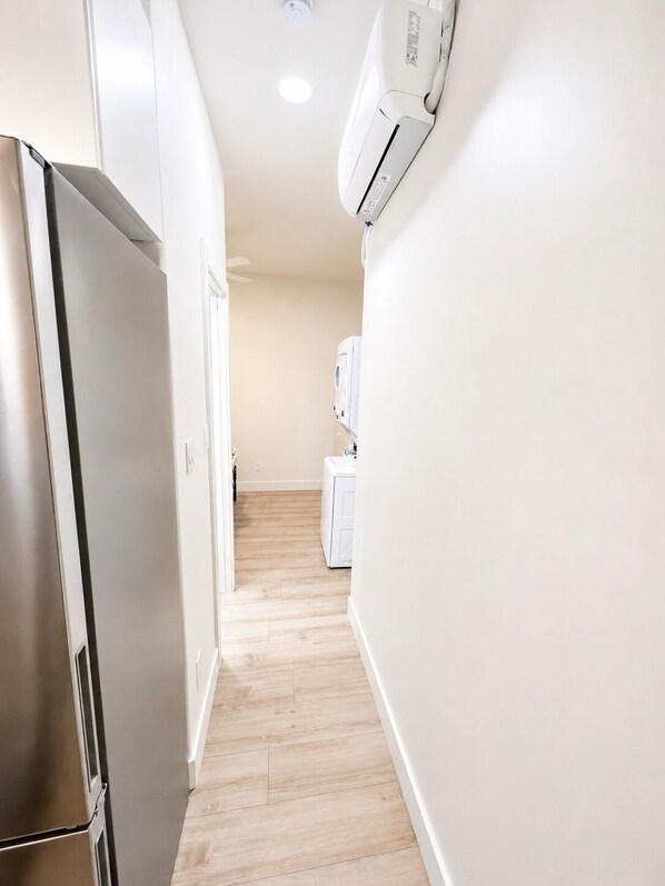 Un pasillo estrecho con un refrigerador de acero inoxidable a la izquierda y una lavadora blanca a la derecha.