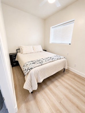 A bedroom with a bed, a nightstand, a window with blinds, and a ceiling fan.