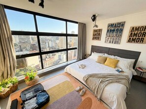 A hotel room with a large window, a bed with pillows, a bedside table with books, and a wall with motivational quotes. - 3027M (São Paulo)