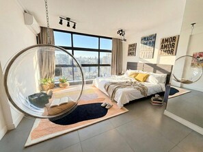 Ein modernes Schlafzimmer mit einem großen Fenster, einem Hängesessel und einem Bett mit Blick auf die Stadt.