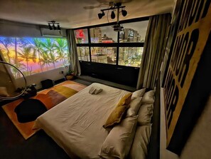 A modern bedroom with a large bed, a desk, and a view of the cityscape through a window. - 3027M (São Paulo)
