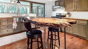 A modern kitchen with a central island, bar stools, wooden cabinets, and a large window providing natural light. - Vermont Escape in Ludlow Village - Okemo (Ludlow)