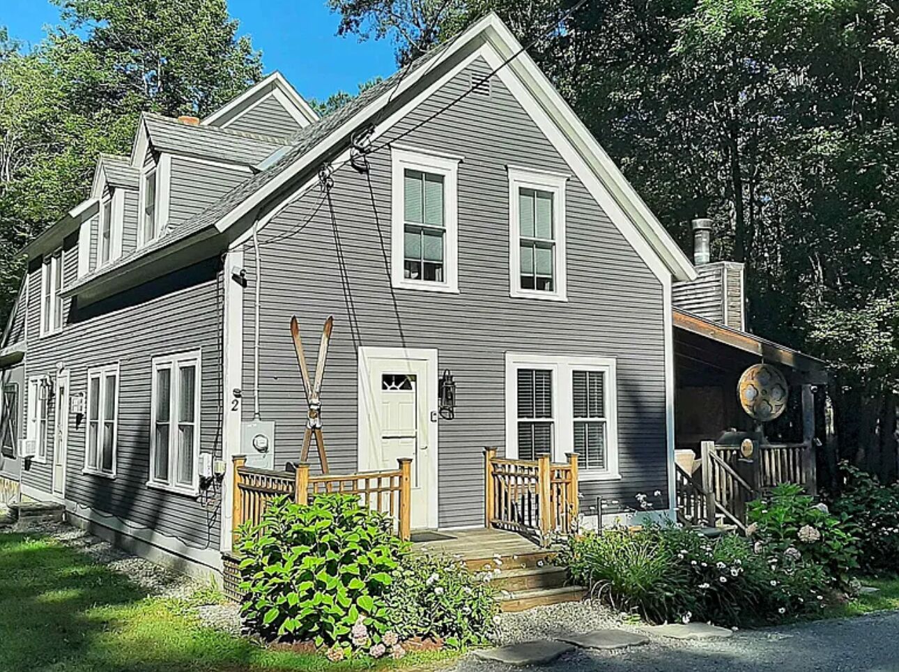 A two-story house with a front porch, a wooden fence, and a garden.