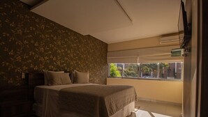 A bedroom with a bed, a window, and a TV on the wall.
