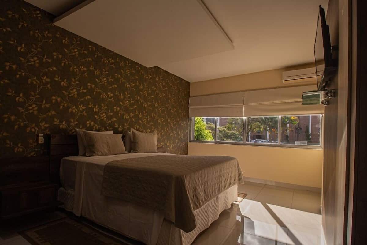 Un dormitorio con una cama, una ventana y un televisor en la pared.