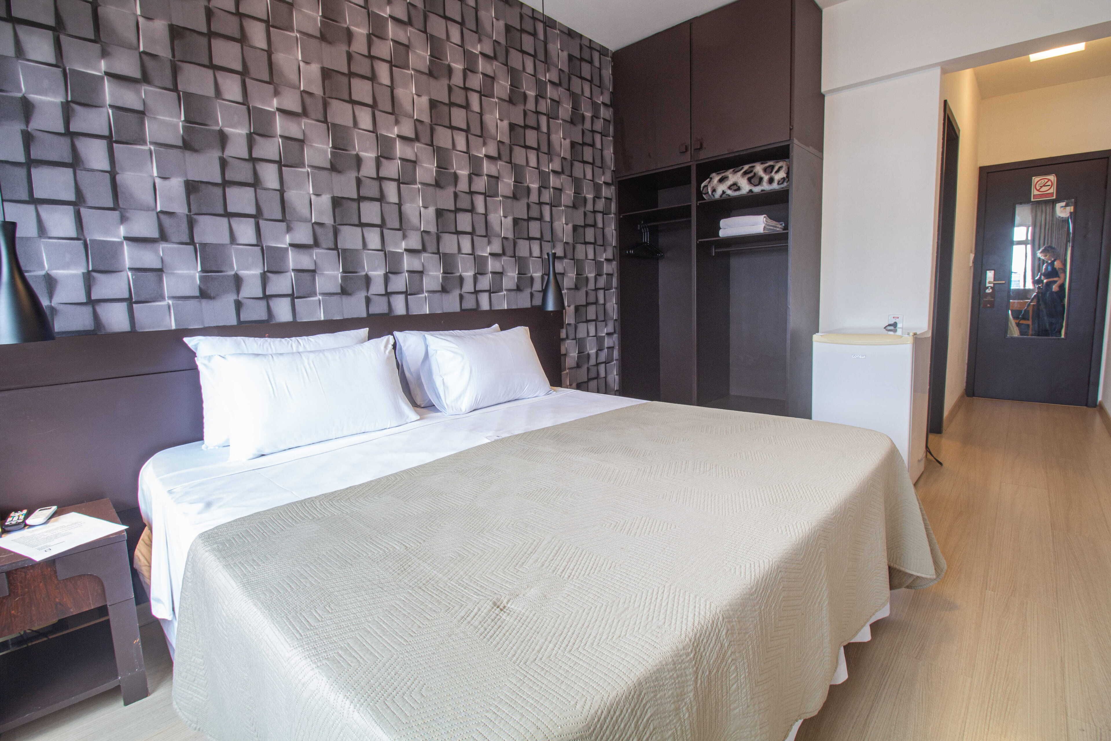 A hotel room with a large bed, a headboard with a textured design, a wardrobe, and a mirror in the corner.