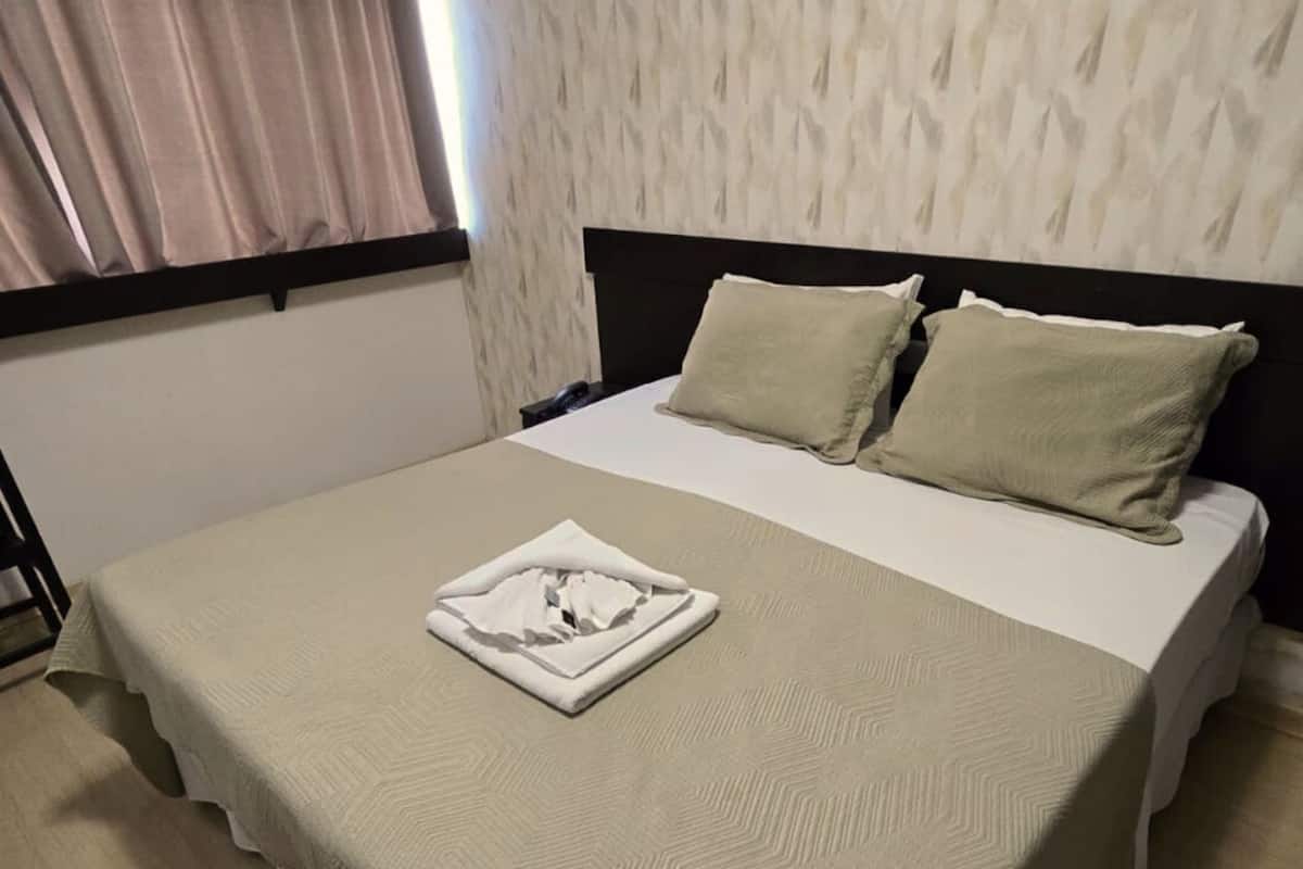 Una cama bien tendida con una colcha y almohadas estampadas, una mesita de noche y un papel tapiz decorado.
