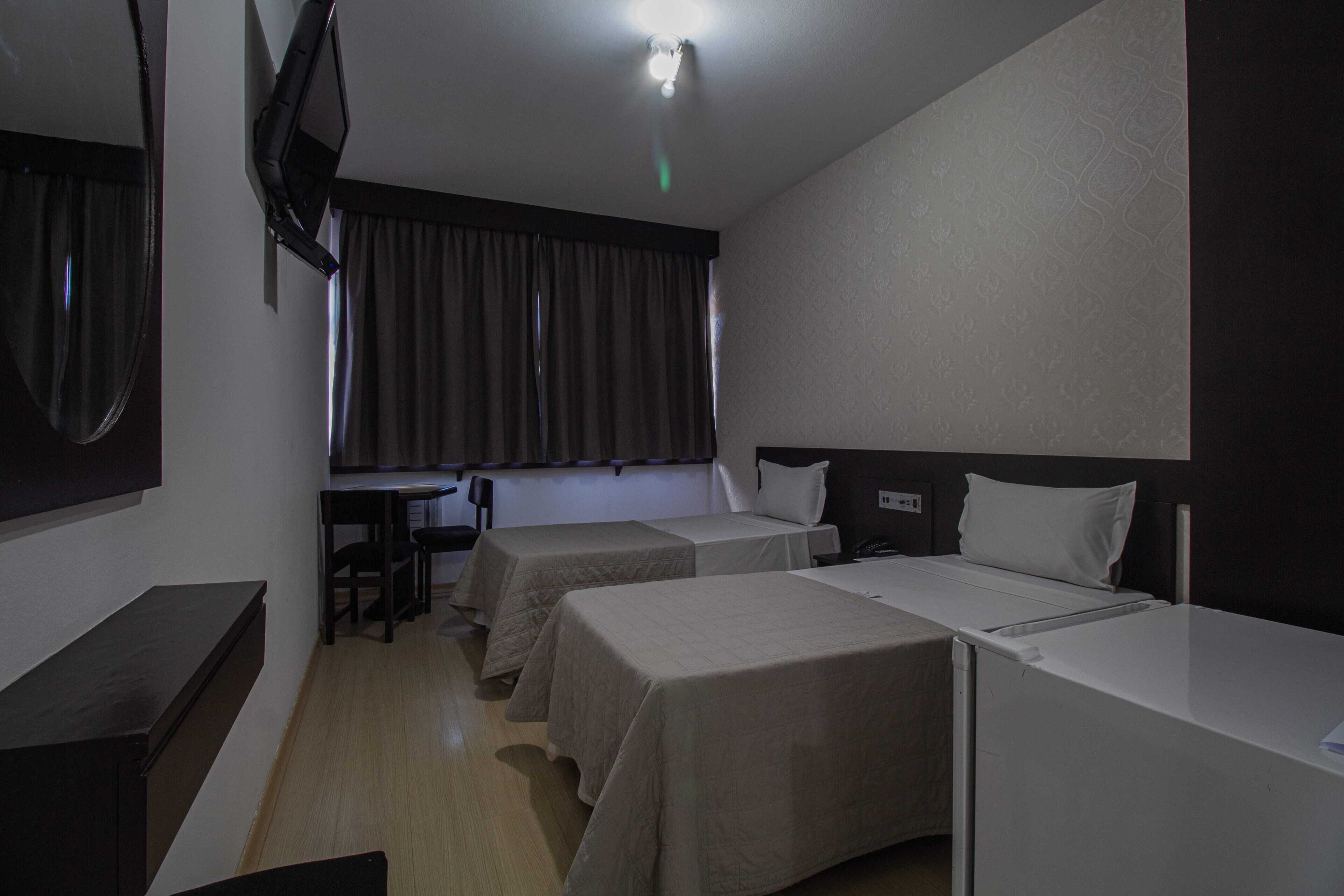 A hotel room with two single beds, a desk, a chair, a TV, and a window with curtains.