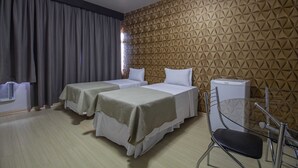 A hotel room with two beds, a chair, a desk, and a radiator.