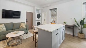 Un salon moderne comprenant un canapé, une table basse, un téléviseur, un lave-linge et un îlot de cuisine.