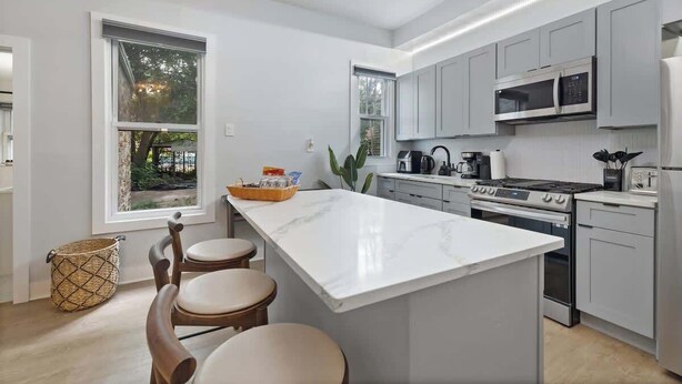 Une cuisine moderne avec des meubles gris, un grand îlot central doté de tabourets, un four à micro-ondes, une cuisinière et un réfrigérateur.