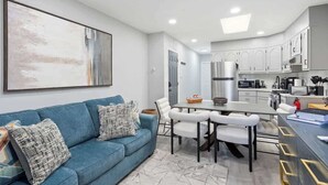 Eine moderne Küche mit weißen Schränken, ein Essbereich mit einem blauen Sofa und ein großes abstraktes Gemälde an der Wand.
