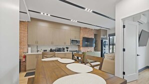 Une cuisine moderne avec des meubles en bois, un mur d’accent en briques et un coin repas comprenant une table et des chaises en bois.
