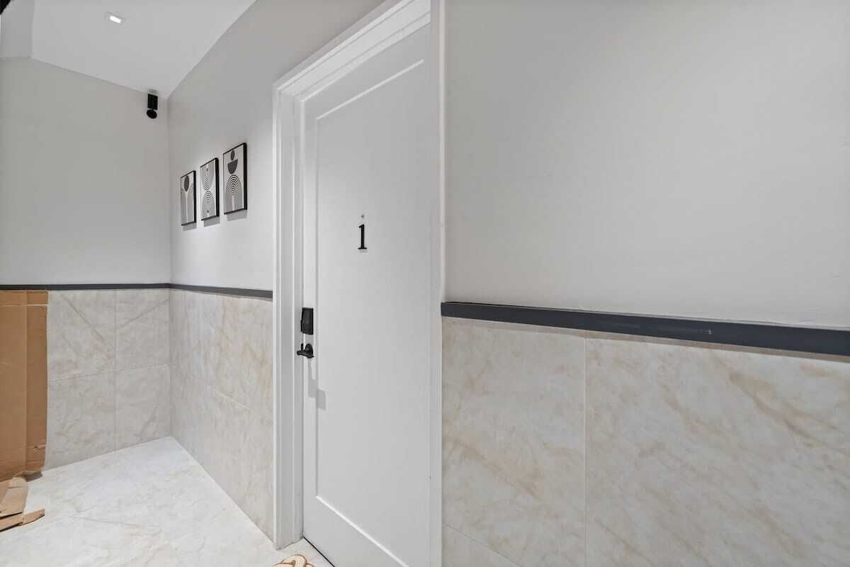 A hallway with white walls, a door marked with the number 1, and framed artwork on the wall.