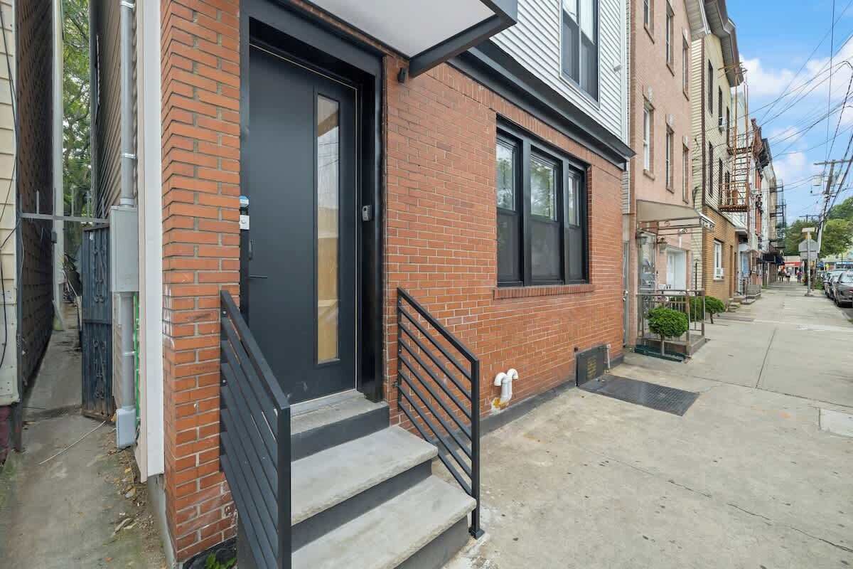 A residential building with a brick facade, a black door, and a small set of steps leading to a black metal railing.