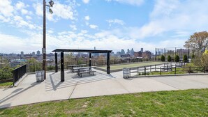 An outdoor seating area with a pergola, benches, and a view of the city skyline. - Modern Studio < 20 Min to NYC w/ Fast WiFi (Jersey City)
