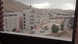 Vista desde una ventana de un edificio con varios pisos, una calle con coches y un paisaje montañoso al fondo.