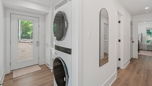 A laundry room with two washing machines, a large mirror, and a door leading to an outdoor area.