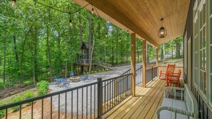 A wooden deck with a railing, outdoor seating, and a view of a forested area.