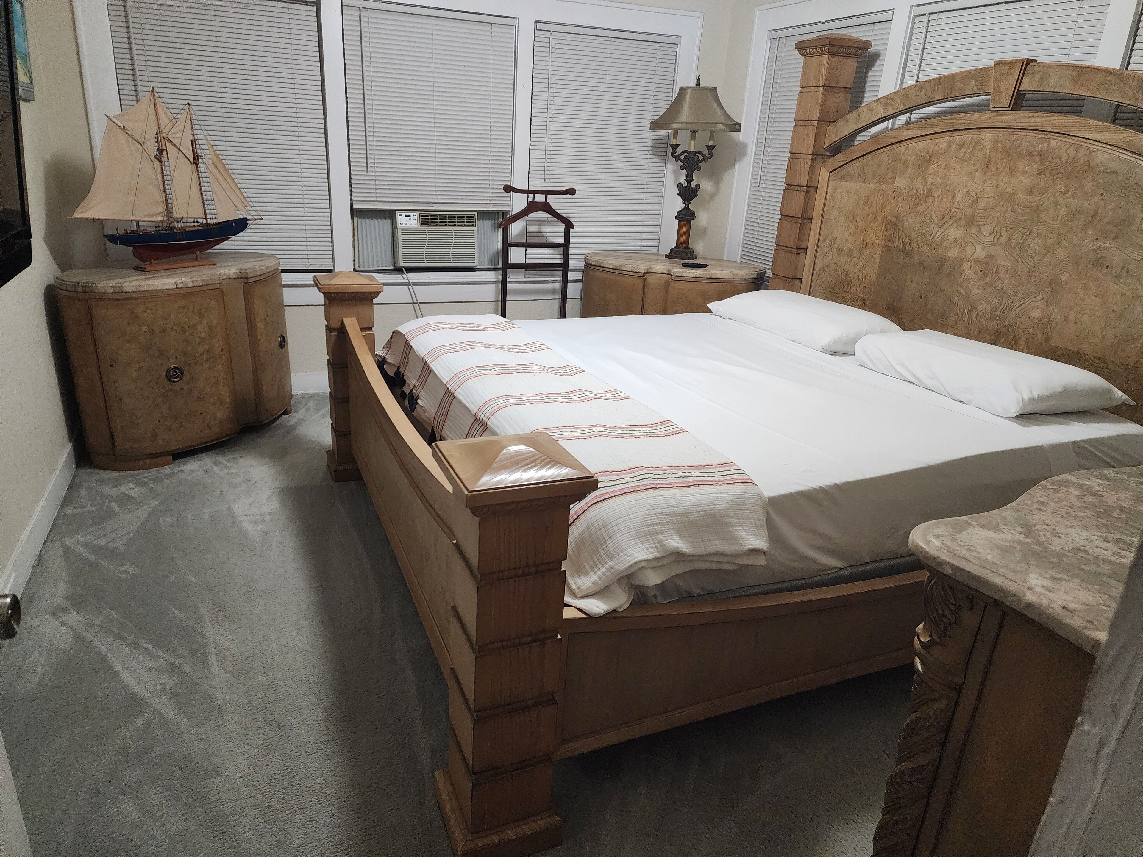 Una cama de madera con cabecera, una mesita de noche, una lámpara y un modelo de barco sobre una pequeña mesa.