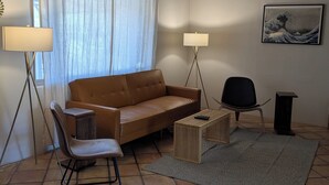 Una sala de estar con un sofá marrón, una mesa de centro de madera, una silla negra y una lámpara.