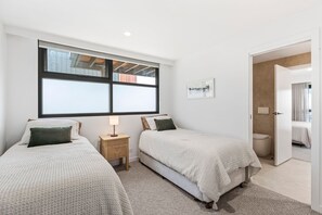 Ein Schlafzimmer mit zwei Betten, einem Nachttisch, einem Fenster und einer Tür zu einem Badezimmer.