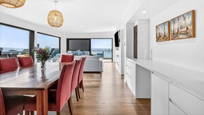 A modern kitchen with white cabinets and a dining area with a wooden table and red chairs. - Teremoana (Lorne)