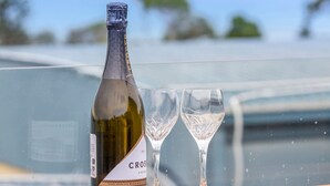 A bottle of wine and two glasses on a table with a view of the ocean. - Teremoana (Lorne)