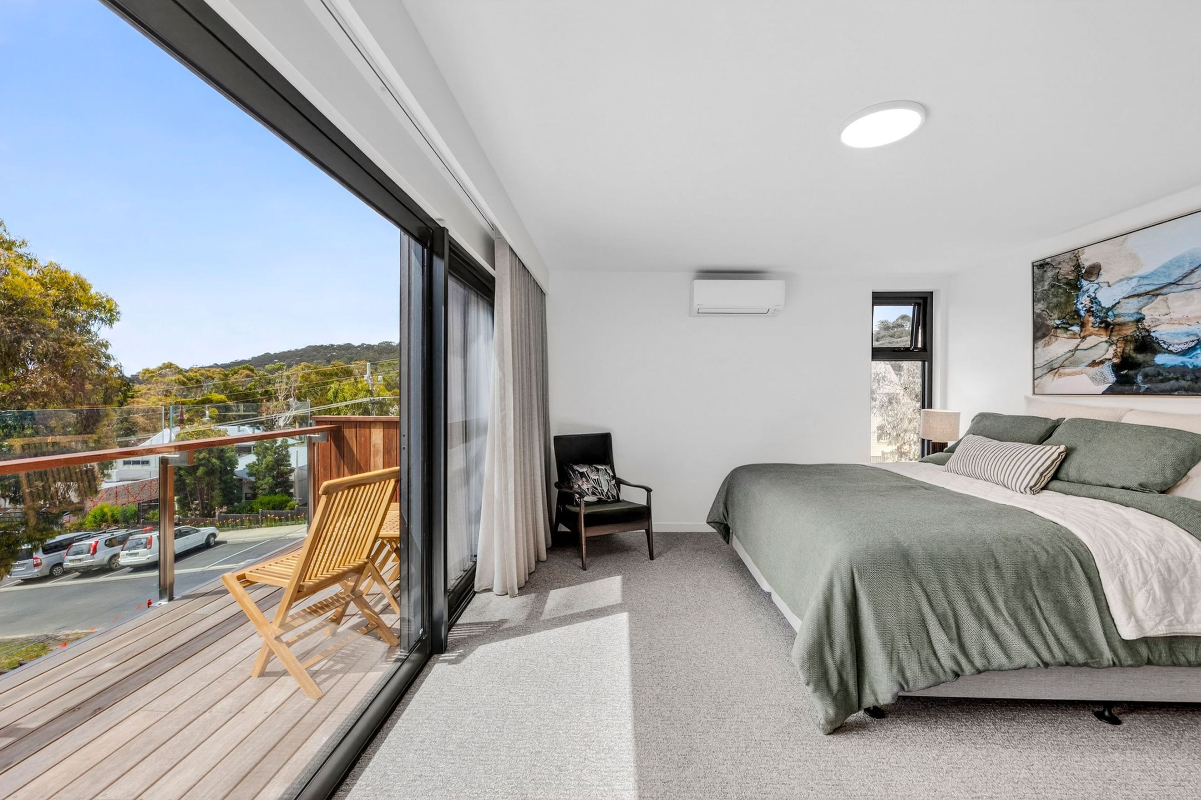 A modern bedroom with a balcony, a bed with green bedding, a chair, and a painting on the wall.