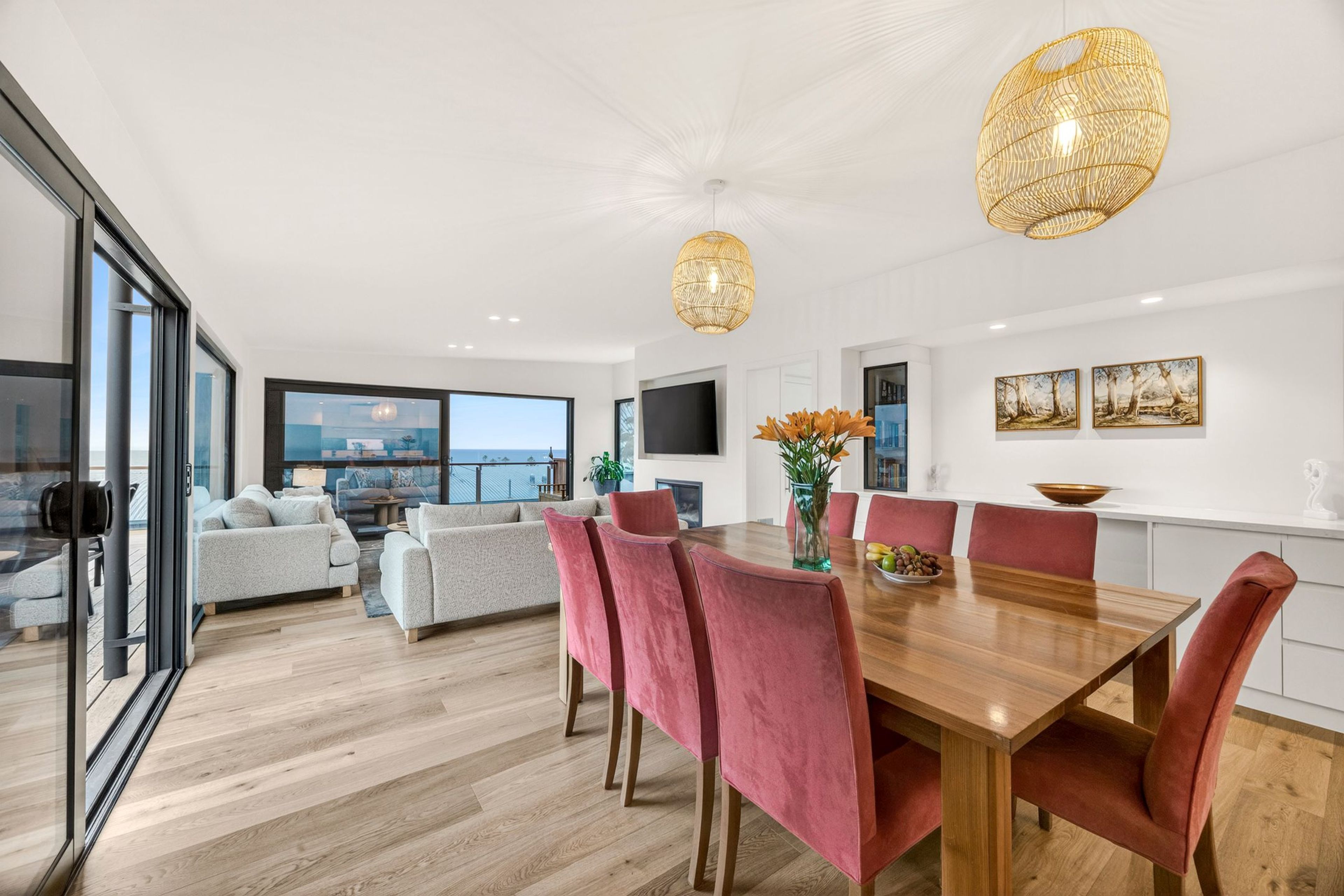 A modern dining area with a wooden table, red upholstered chairs, and a large window overlooking a cityscape.
