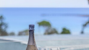 A bottle of champagne on a table with a glass, overlooking a body of water and greenery. - Teremoana - the heart of Lorne (Lorne)