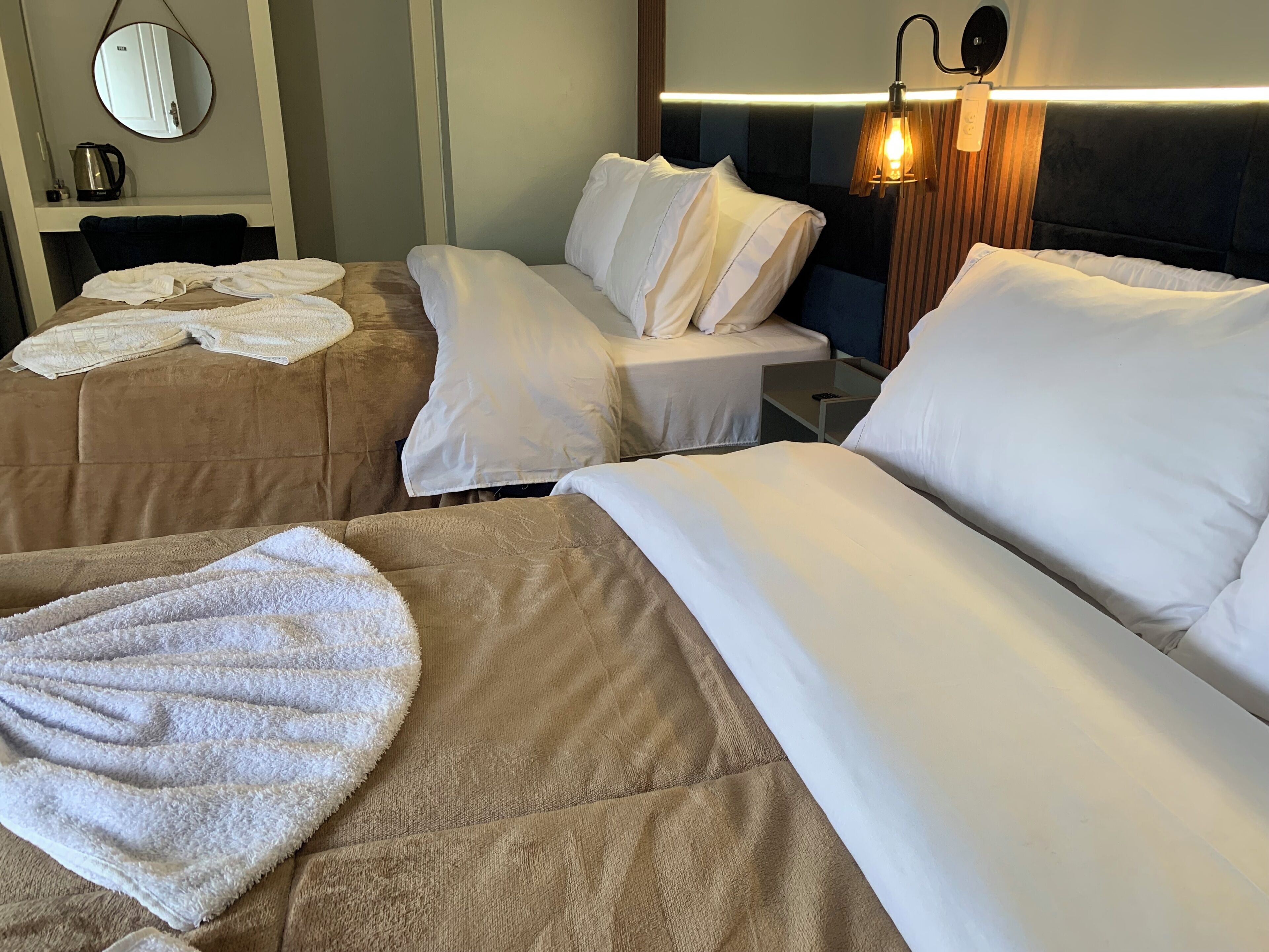 Una habitación de hotel con dos camas, un espejo redondo, una mesita de noche con una lámpara y un aplique de pared.