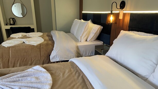 Una habitación de hotel con dos camas, un espejo redondo, una mesita de noche con una lámpara y un aplique de pared.