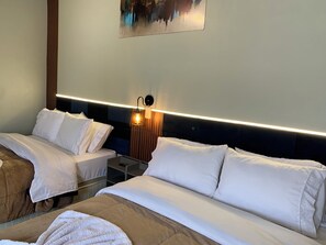 A hotel room with two beds, a nightstand, a wall-mounted lamp, and a painting.