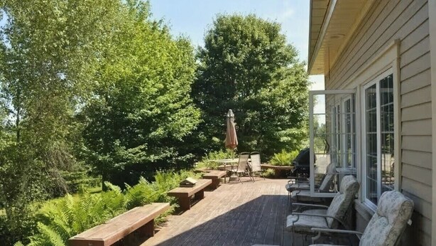 Una terraza de madera con mobiliario exterior y un gran árbol al fondo.