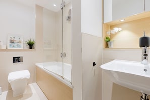 A modern bathroom with a bathtub, toilet, shower, and sink. - Colourful 1BDR Canalside Flat in East London (Greater London)