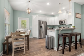 A modern kitchen with white cabinetry, stainless steel appliances, and a central island with bar stools. - Cozy 2 Bedroom Atlas Cottage near Milton FL (Milton)